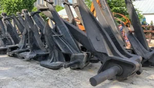 Anclas de grandes dimensiones de diferentes diseños apiladas en un recinto industrial.