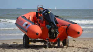 Embarcación neumática semirrígida naranja con motor fueraborda de 60 CV sobre un remolque en la playa.