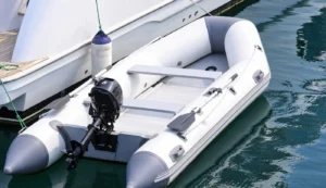 Embarcación neumática blanca con motor fueraborda junto a un velero, como exemplo de motor para neumática